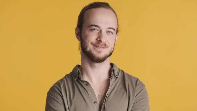 Young attractive bearded man dressed in casual wear looking confident smiling on camera over yellow background. Face expression