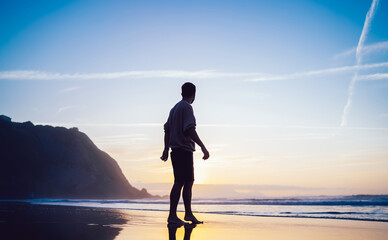 Unrecognizable man standing on sea beach looking at sunrise