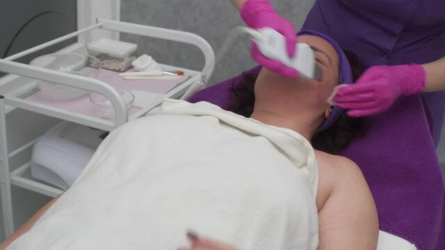 The beautician performs cavitation peeling of the cheeks using an ultrasound device.