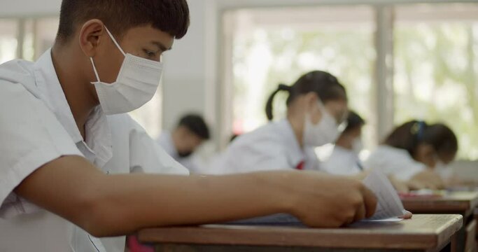 Slow motion scene of Asian high school students in a white school uniform wearing the masks to do final exams in the midst of Coronavirus disease 2019 (COVID-19) epidemic.