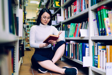 Woman sitting among bookshelves and reading book