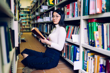 Asian woman sitting with book between bookcases