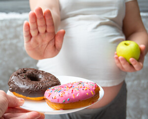 Close-up of a pregnant woman holding a green apple in her hands, refusing donuts. Healthy food...