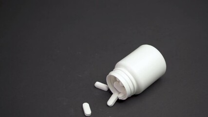 Close up woman s hand falls out Prescription bottle filled with white pills spills in to scatter contents. White pills are spilling on the black medical table. Concept of healthcare and medicine 4k - Powered by Adobe