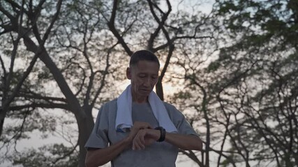 asian senior elderly man touching smart watch activity tracker at park under tree. finger tapping sport watch for calories and heart rate information. slow motion orbit shot. health care concept. - Powered by Adobe