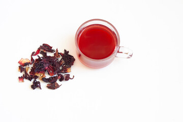 Red hibiscus tea in a glass transparent cup and dried hibiscus flowers on a white background, top view