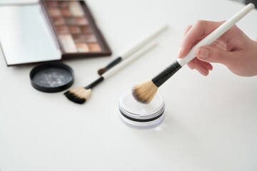 Makeup brushes. A woman's hand applies makeup to the skin. The brush comes in white powder for applying makeup