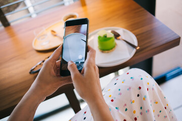 Faceless woman showing photo on smartphone screen in cafeteria