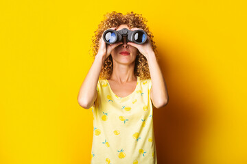 curly-haired girl looks through binoculars on a bright yellow background.