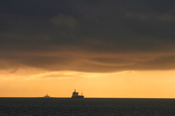 cargo sur la mer avec un phare au loin et le coucher de soleil pr&egrave;s du port de Lisbonne au Portugal
