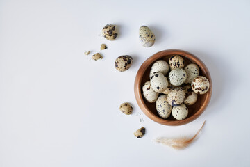 quail eggs in a wooden bowl painted with a feather on a white table. Easter concept Copy space
