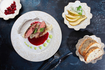 Duck breast with cranberry sauce and sweet pear on a white plate. Top view. The concept of the restaurant menu. Blue background.
