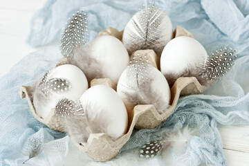 Fototapeta na wymiar White eggs with feathers in carton box. Easter theme