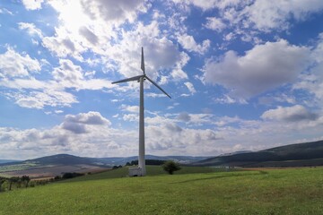 Fototapeta na wymiar Wind power plant in landscape with turbine between the clouds at blue sky