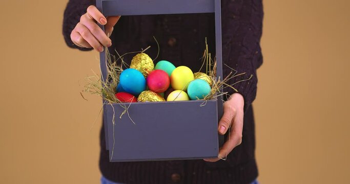 Women's hands giving wooden basket full of easter festive eggs, close up studio video 