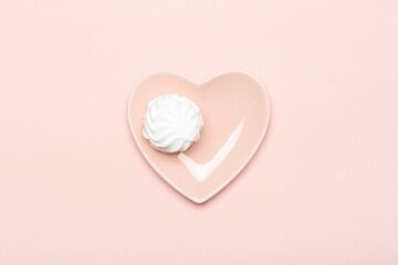 White marshmallow on a pink plate in the shape of a heart on a pink background
