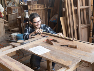 Handsome Caucasian carpenter using a tape measure for measuring woodwork in the carpentry workshop. Manufacture of wood products...