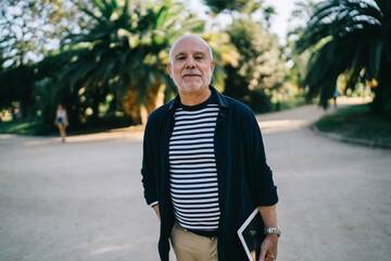Obraz premium Half length portrait of aged senior traveller with modern touch pad gadget looking at camera during free time in city, casual dressed male tourist 60s with digital tablet posing on retirement