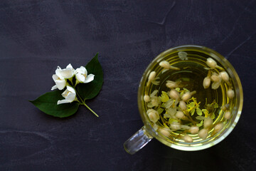 cup of Jasmine tea. Cup of hot herbal tea with jasmine fresh flowers on a black table. Healthy lifestyle. glass cup of green tea with leaves on a black background. Hot drinks. copy space. top view