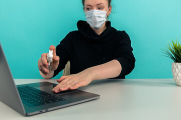 Woman in the mask desinfecting hands and laptop at home.