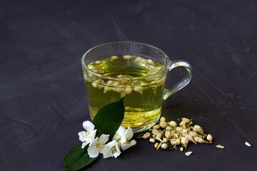 Jasmine tea. Cup of hot herbal tea with jasmine fresh flowers on a black table. Healthy lifestyle....