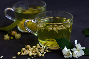 Jasmine tea. two cups of hot herbal tea with linder flowers on a black table. Healthy lifestyle. glass cups of green tea on a black background. Hot drinks.