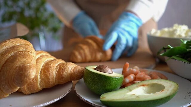 Close-up of a chef in gloves preparing a croissant sandwich