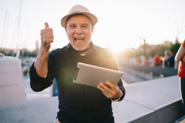 Half length portrait of cheerful male tourist with modern gadget showing OK during positive leisure...