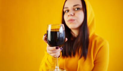Relaxed young woman poses with glass of red wine on yellow background. Adult happy brunette resting with alcohol in her weekend.