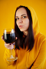 Relaxed young woman poses with glass of red wine on yellow background. Adult happy brunette resting with alcohol in her weekend.