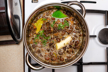 Mushroom soup with vegetables boiled in a metal pot on a gas stove, top view.
