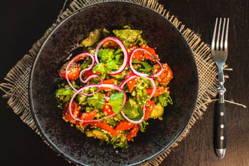 Quinoa salad with tomatoes, avocado, paprika and parsley on black stone plate. Top view.