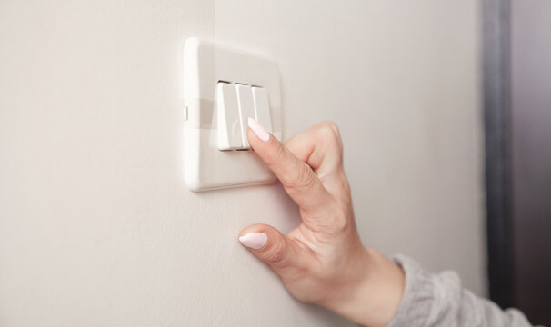 Female hand turning an electricity light switch on the wall.