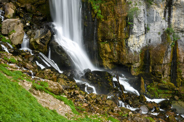 Fototapeta na wymiar Beautiful long exposure photo of a waterfall in switzerland rushing down a cliff and bursting onto a steep rocky mountainside.