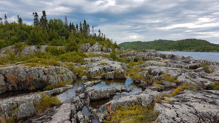 Senic landscape of the Lake Superior coastline in the Pukaskwa Nationalpark. A rocky hillside covered with bushes and ponds next to a mixed forest.