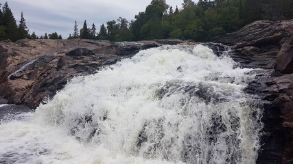 Huge white waterfall rushes down a rocky hillside