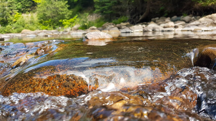 Closeup of a stone bathed by a creek creating a scenic little transparent waterfall.