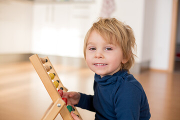 Sweet blond preschool child, toddler boy, playing with abacus at home,construction on the floor behing