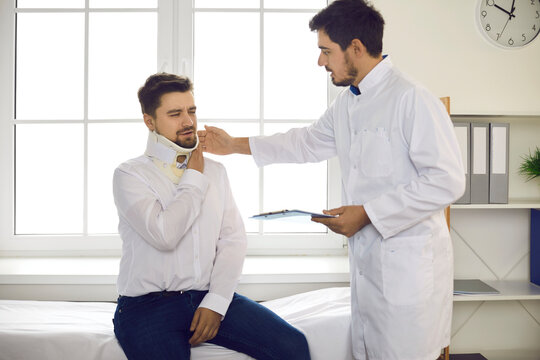 Young man with neck injury telling doctor about his troubles with grimace of pain and suffering. Professional traumatologist or physiotherapist helping male patient who's wearing cervical collar