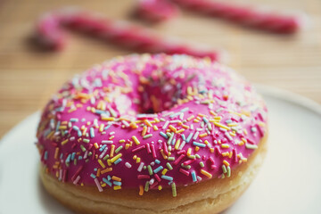 macro photo of a donut under pink glaze with multi-colored sprinkles