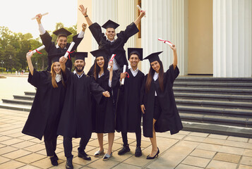 Group of happy smiling cheerful university graduates posing with dimplomas in raised hands over...