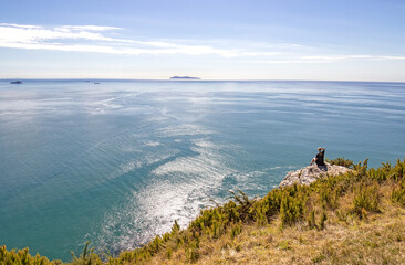 Tauranga, New Zealand. Hiker sitting resting enjoying Panoramic sea view from Mount Maunganui. Tauranga is a major cruise ship outdoor nature destination on northern island. Person materially altered