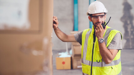 Professional cargo worker talks on portable radio to contact another worker . Factory and warehouse...