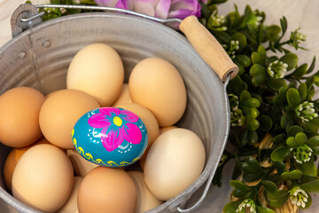 Natural color chicken eggs from the Easter decoration. In the center, a hand-painted Easter egg. Flower ornaments on the outside. All on a wooden background.