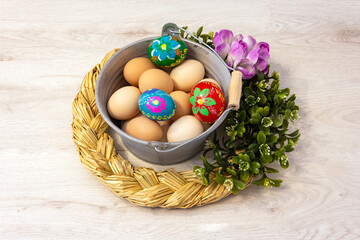 A beautiful Easter, decorative composition with a metal bucket filled with chicken eggs and Easter eggs. Hand-painted colorful Easter eggs. Decorative buckets outdoors with flowers on a wooden backgro