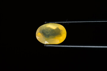 Yellow opal in tweezers on a black background