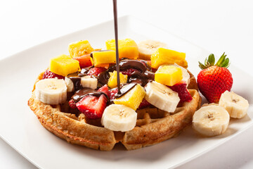 Waffle topped with strawberry, banana and orange fruits and dark chocolate