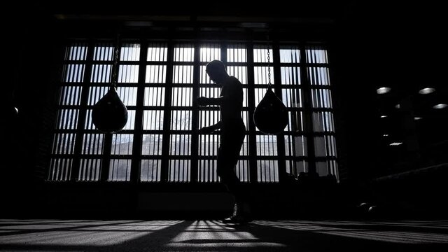 The silhouette of a male boxer in a boxing gym, he jumps on a skipping rope.