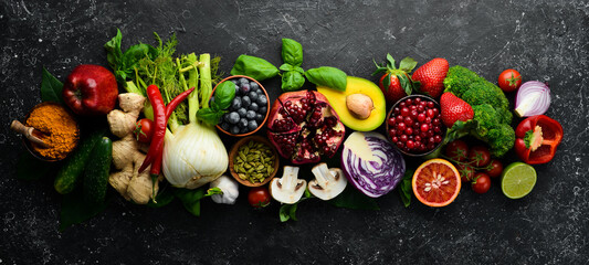Fresh vegetables and fruits: fennel, avocado, pomegranate, berries, cabbage and basil. Organic healthy vegan food. On a black stone background.