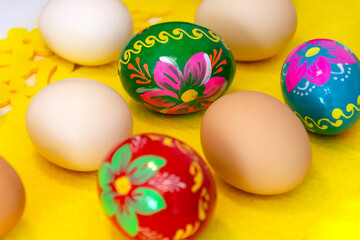 Easter eggs and chicken eggs in a natural color on a yellow tablecloth. Colorful Easter ornament with hand-painted eggs.
